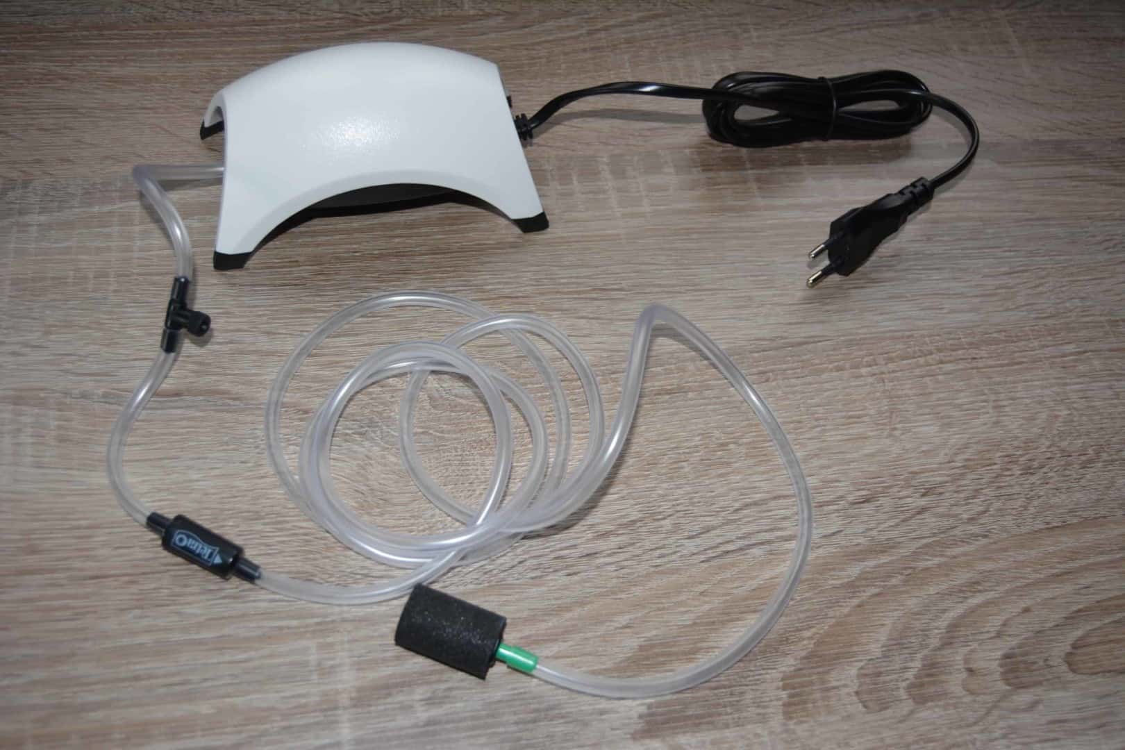Weiße Luftpumpe mit Kabel, Luftschlauch, Rückschlagventil und Ausströmstein auf Holzboden, Hilfe bei Sauerstoffmangel.
